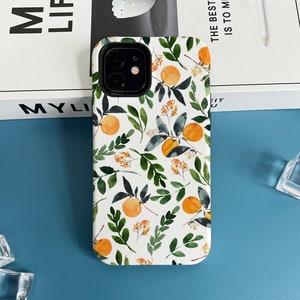 Puede incluir: Carcasa de teléfono blanca con un patrón floral de flores de naranja y hojas. La carcasa tiene un recorte para el objetivo de la cámara.