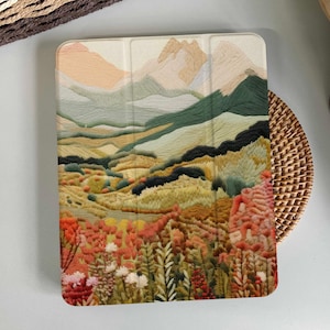 May include: A colorful embroidered landscape scene with mountains, hills, and fields of flowers. The image is on a white background and is perfect for a phone case or tablet cover.