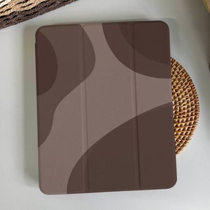 May include: An iPad case with an abstract pattern in shades of brown and beige, featuring a smooth, textured finish.
