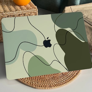 Könnte beinhalten: Ein Laptop mit einem abstrakten Design in Grün und Beige. Das Design zeigt schwarze Linien und ein schwarzes Apple-Logo.