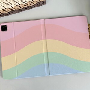 May include: A pastel rainbow-colored case for a tablet or iPad. The case is closed and has a soft, textured finish.