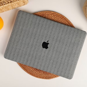 May include: A gray laptop computer with a textured fabric cover. The laptop is sitting on a woven wicker coaster.
