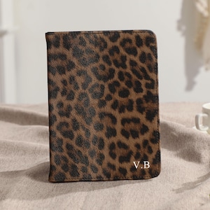 May include: A rectangular brown and black leopard print cover with the initials "V.B" in the bottom right corner. The cover is sitting on a neutral-colored surface. A white teacup and greenery are in the background.