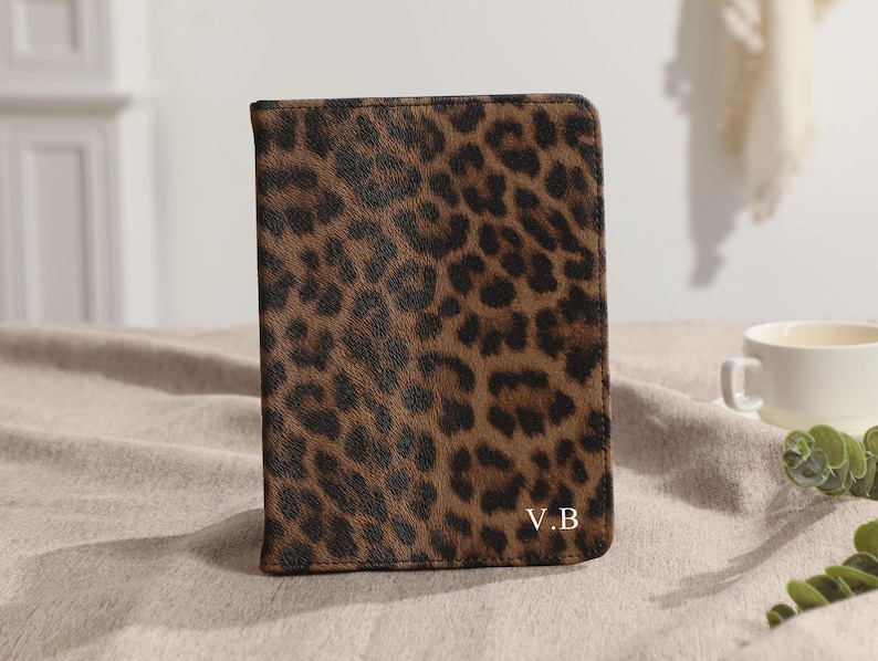 May include: A rectangular brown and black leopard print cover with the initials "V.B" in the bottom right corner. The cover is sitting on a neutral-colored surface. A white teacup and greenery are in the background.