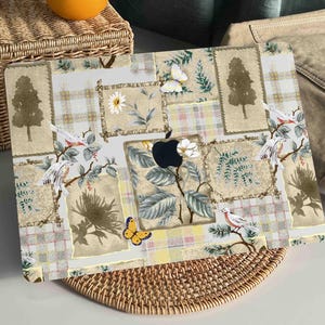 Puede incluir: Una piel para portátil con un diseño de patchwork que presenta pájaros, mariposas, árboles y motivos florales en tonos marrones, blancos y verdes.
