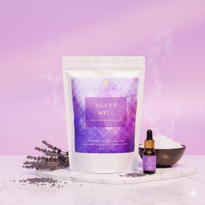 以下が含まれることがあります： 紫色の背景に「SLEEP WELL」と「MAGNESIUM BATH SALTS」の文字が入った白いバッグ。小さなエッセンシャルオイルのボトルとバスソルトのボウルがバッグの隣にあります。ラベンダーの束が左側にあります。