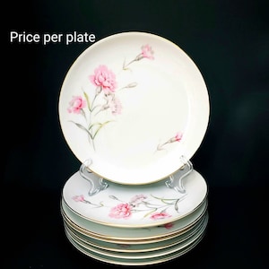May include: A stack of six white ceramic plates with a gold rim and a pink carnation floral design.  The text "Price per plate" is visible at the top of the image.