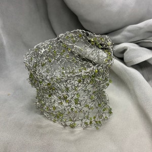 Puede incluir: Un collar gargantilla de alambre plateado con cuentas verdes tejidas en el diseño.