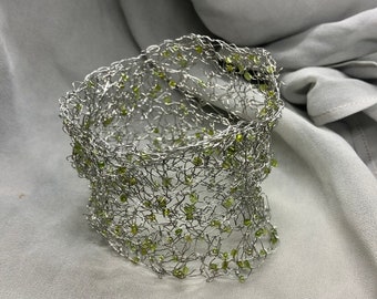 May include: A silver wire choker necklace with green beads woven into the design.