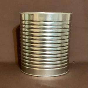 May include: A cylindrical, silver-colored metal can with horizontal ridged lines. The can has a shiny, reflective surface and a simple, utilitarian design. The can is likely used for food storage or packaging.