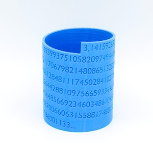 Puede incluir: Un cilindro de plástico azul con los dígitos de pi impresos en él. El cilindro tiene aproximadamente 7,6 cm de alto y 2,5 cm de diámetro. Los números comienzan con "3, 14159265..."