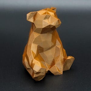 May include: A geometric, golden-brown bear figurine. The bear is sitting, with a faceted design creating a polygonal appearance. The figurine is made of a material with visible layered texture.