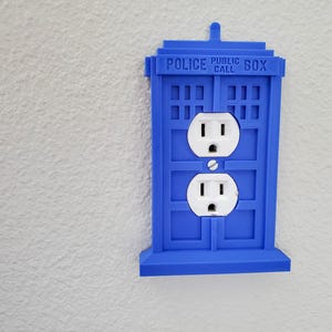 May include: A blue plastic outlet cover shaped like a police telephone box with the text "POLICE PUBLIC CALL BOX".