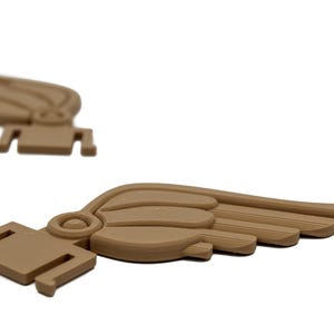 May include: Two brown plastic wings with a detailed design. The wings are curved and have a textured surface.