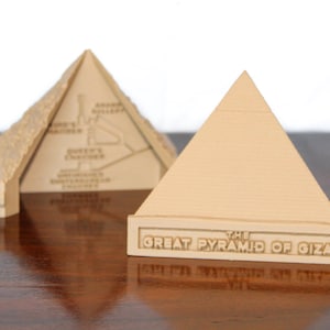 May include: Two miniature models of the Great Pyramid of Giza. One model is open to reveal a detailed interior map. The other model has the text "The Great Pyramid of Giza" inscribed on the base.