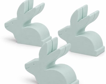 May include: Three pale mint green rabbit-shaped figures, each featuring a smooth, solid silhouette with upright ears and a small slit at the top. These decorative items are positioned in a group, displaying a consistent matte finish and simple, clean lines.