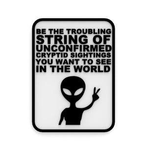 May include: Black and white sign with the text "Be the troubling string of unconfirmed cryptid sightings you want to see in the world."  A black alien with a peace sign is below the text.