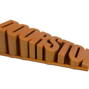Pode incluir: Um calço de porta castanho, impresso em 3D, em forma da palavra "DOORSTOP". As letras são grossas e quadradas, com uma textura canelada. O calço de porta está inclinado, com as letras a diminuir em altura.