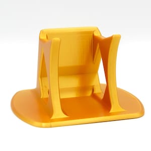 May include: A bright yellow phone stand with a curved design. The stand has a wide, flat base and a cradle to hold a phone. The stand is made of a solid material and has a smooth finish. The stand is designed to hold a phone in a vertical position.