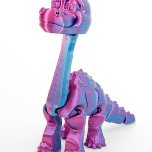 May include: A 3D printed dinosaur toy with a pink and blue iridescent finish. The dinosaur has a long neck, a small head with large eyes, and a long tail. It has four legs and is standing on a white surface.