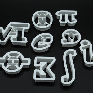 May include: Set of ten white plastic cookie cutters shaped like mathematical symbols, including pi, integral, and the square root of 2.