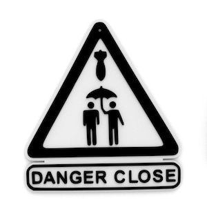 May include: A black and white sign with a triangular shape and the words "DANGER CLOSE". The sign features a graphic of two figures under an umbrella, with a bomb above them.