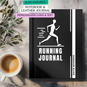 Może przedstawiać: Czarny dziennik biegacza z białym graficznym przedstawieniem biegacza i napisem "RUNNING JOURNAL". Dziennik zawiera również biały napis "DAVID MCKENZIE". Dziennik leży na jasnoszarej powierzchni z filiżanką kawy i zielenią.