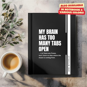 May include: Black and white notebook with the text "MY BRAIN HAS TOO MANY TABS OPEN... 4 of them are frozen, and I have no idea where the music is coming from." and the author's name "JANE MITCHELLS". The notebook is on a light brown surface with a green plant in the background. The text "ALSO AVAILABLE IN NOTEBOOK & VARIOUS COLORS!" is in a red box in the top right corner.