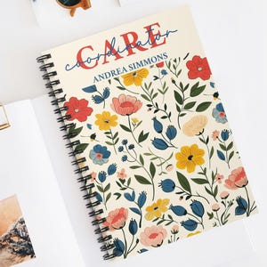 Puede incluir: Un cuaderno con espiral con un diseño floral. La portada presenta las palabras "CARE coordinator" y el nombre "ANDREA SIMMONS". El patrón floral incluye flores rojas, amarillas, rosas y azules con hojas verdes sobre un fondo crema.