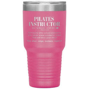 May include: A pink stainless steel tumbler with a silver lid. The tumbler has a white inscription that reads "PILATES INSTRUCTOR [pa- l&auml;-tēz] [in- strək-tər] noun (n) Someone who solves problems you never knew existed in ways that will blow your mind. See also: ninja; badass; legend"