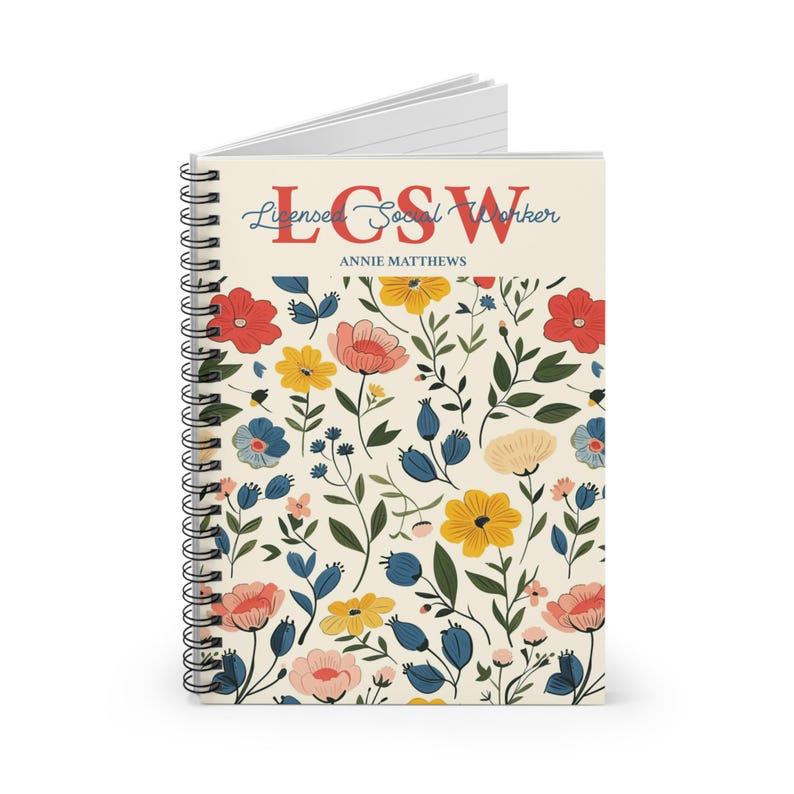 K&ouml;nnte beinhalten: Ein spiralgebundenes Notizbuch mit cremefarbenem Einband und einem Blumenmuster aus roten, gelben, rosafarbenen und blauen Bl&uuml;ten mit gr&uuml;nen Bl&auml;ttern. Der Text lautet LCSW, Licensed Social Worker, und der Name ANNIE MATTHEWS in Rot und Blau.