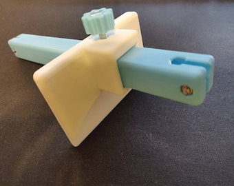 May include: A 3D-printed tool in light blue and off-white. It has a central off-white block with a light blue knob and two light blue arms. The arms have slots and are secured with small screws. The tool is designed for a specific purpose.