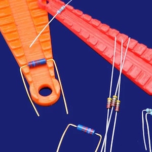 May include: An orange and red electronic component holder with various resistors. The resistors have colored bands and are connected with wire leads. The components are arranged on a dark blue background.