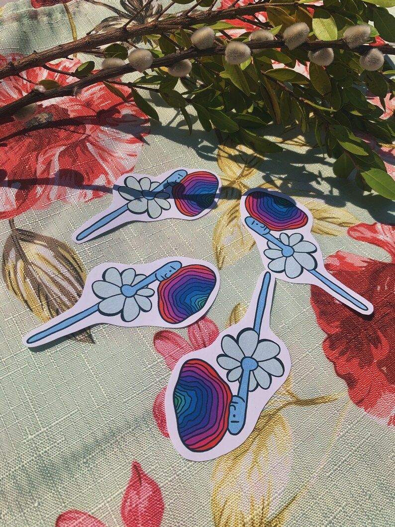 May include: Four colorful stickers featuring a psychedelic mushroom with a face and a daisy. The mushroom is a rainbow of colors, including red, orange, yellow, green, blue, and purple. The daisy is light blue.