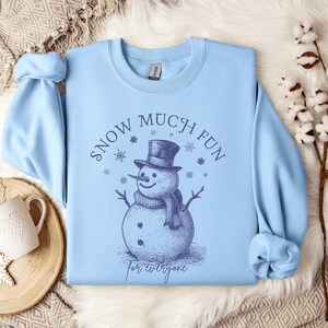 May include: Light blue sweatshirt with a snowman graphic and the text "Snow Much Fun for Everyone".