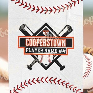Puede incluir: Manta blanca con temática de béisbol. Presenta una pelota de béisbol, bates cruzados y el texto "COOPERSTOWN PLAYER NAME ##". Diseño de costura de béisbol roja a lo largo de los bordes superior e inferior. Disponible en 127x152 cm y 152x203 cm.