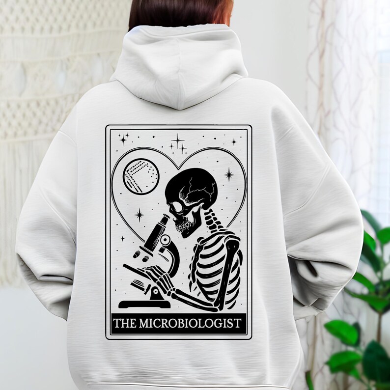 May include: White hoodie with a black and white graphic on the back. The graphic features a skeleton looking through a microscope, inside a heart shape, with the text "THE MICROBIOLOGIST" at the bottom.