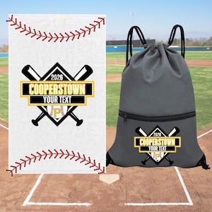 May include: A white rectangular towel with red baseball stitching patterns and a dark gray drawstring backpack. Both items feature a graphic of two crossed baseball bats, a baseball with a letter P, and the text 2026 COOPERSTOWN YOUR TEXT.