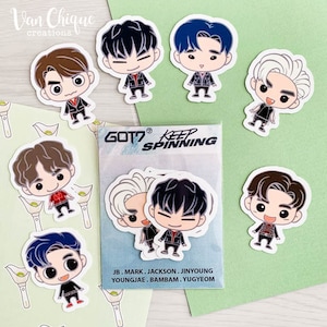 May include: A set of nine Got7 K-pop band member stickers. Each sticker features a cartoon illustration of a different band member. The stickers are printed on white paper and have a glossy finish. The stickers are packaged in a clear plastic bag with the band's name and logo printed on the front. The text on the bag reads "GOT7 Keep Spinning".