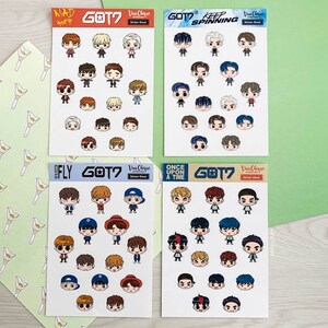 May include: Four sheets of stickers featuring cartoon illustrations of the K-pop group GOT7. Each sheet has a different theme: "Mad", "Keep Spinning", "Fly", and "Once Upon a Time". The stickers are printed on white paper with a glossy finish.
