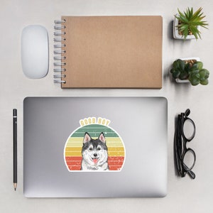 May include: A vintage-style sticker featuring a husky dog with the text "GOOD BOY" in a retro font. The dog is depicted in a watercolor style against a colorful sunset background.