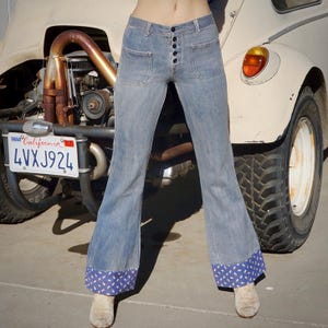 Peut inclure: Jean bleu clair avec une braguette boutonnée et deux poches avant. Le jean a une jambe évasée avec un revers à motifs bleus et blancs. La plaque d'immatriculation californienne indique 4VXJ924.