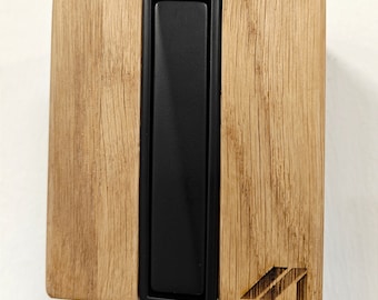 May include: A black rectangular switch plate with a wooden frame. The frame is made of light brown wood with a natural grain pattern. The switch plate is mounted on a white wall.
