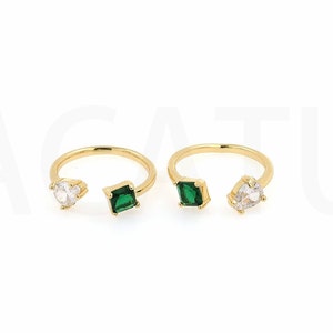 May include: Two gold rings with green and clear stones. The rings are open and have a simple design.