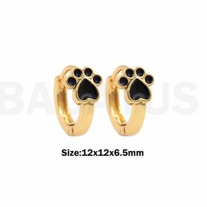 Puede incluir: Un par de pendientes de aro de oro con dijes de huella de pata negra. Tamaño: 12x12x6,5 mm.