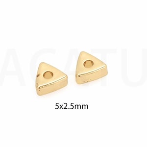 May include: Two gold triangle-shaped beads with a hole in the center. The beads are 5mm x 2.5mm.