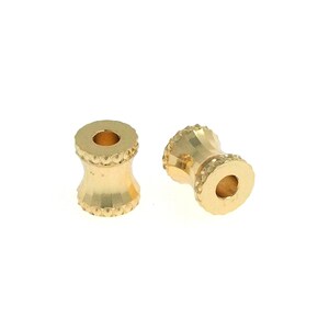 May include: Two gold-colored metal beads with a textured design. The beads have a round hole in the center.