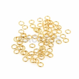 Puede incluir: Un montón de anillos de salto dorados, un tipo de hallazgo de joyería utilizado para conectar cadenas, cordones y otros componentes de joyería.