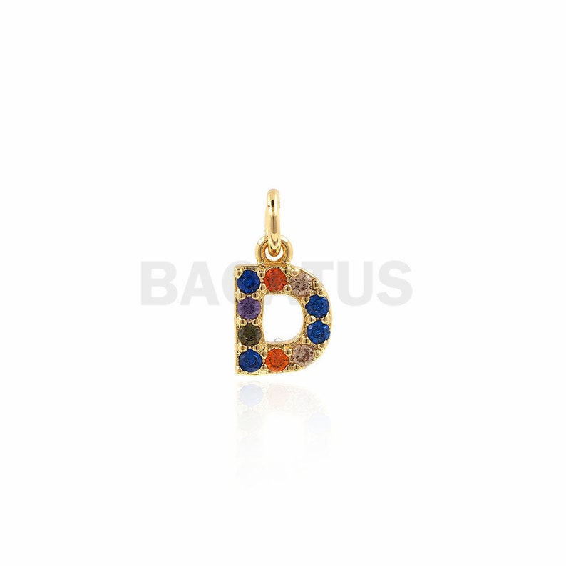 Puede incluir: Encanto de oro en forma de la letra D, con piedras preciosas de colores alrededor de los bordes.