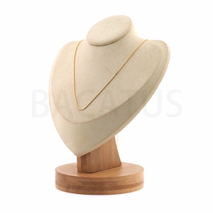 Può includere: Una collana a catena dorata esposta su un busto in velluto beige con una base in legno.